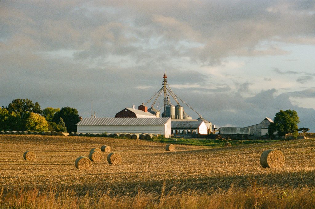 Industrial Photographer 5 Commercial agriculture images showing a farm late in the day. Hay bails line the foreground and out buildings in the background.