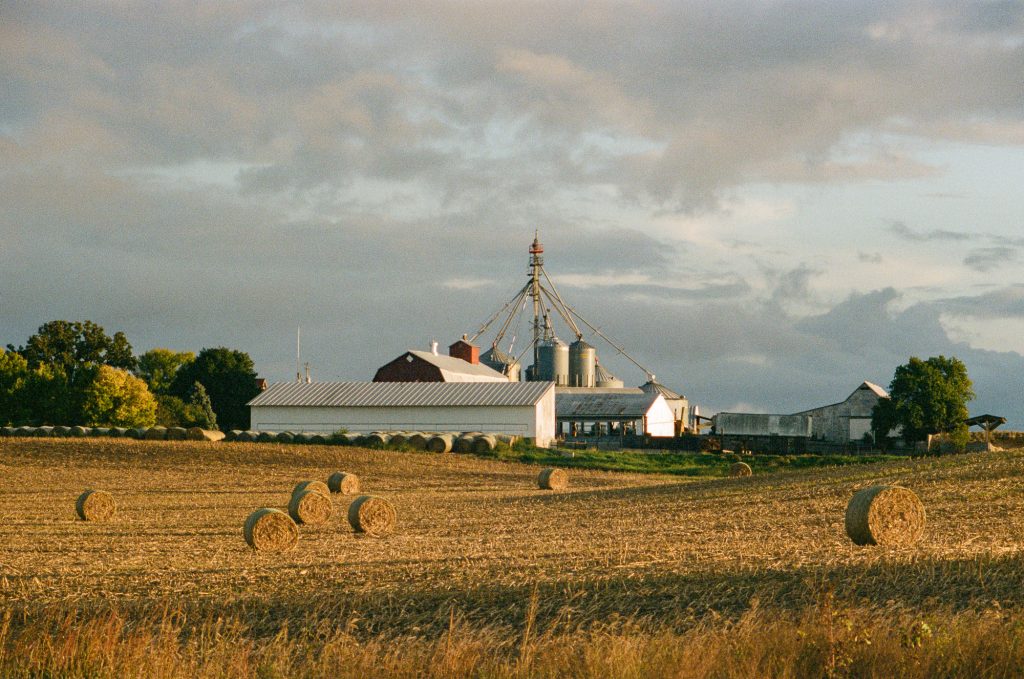 Commercial agriculture images showing a farm late in the day. Hay bails line the foreground and out buildings in the background.